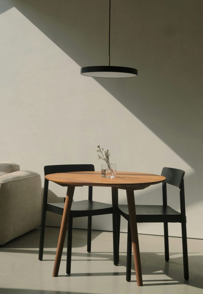 A minimalist bistro table like this one offers a sleek, understated solution for compact dining areas or quiet corners. With its smooth round top and slender black legs, it pairs effortlessly with simple chairs and neutral