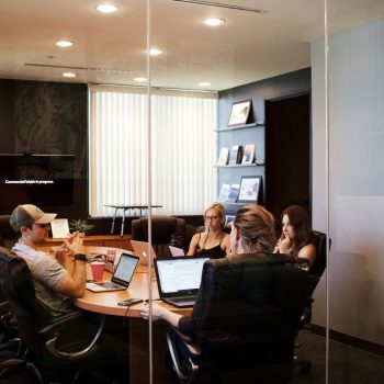 A traditional boardroom table setup, this piece is large and surrounded by high-back executive chairs, ideal for formal business meetings. The room features modern lighting and built-in shelving, suggesting a corporate env